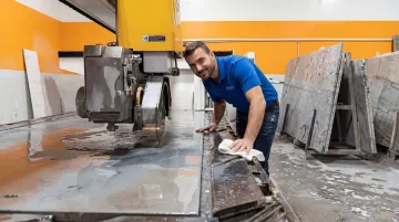 Stone fabrication bridge saw operator performing daily visual inspection and cleaning