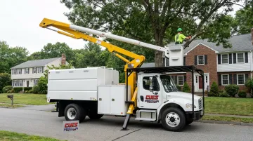 Arborist in bucket truck platform safely trimming large tree canopy near structures