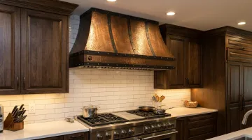 Custom metal wall-mount canopy range hood in copper finish above kitchen range