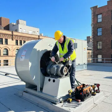HVAC technician repairing a rooftop exhaust fan on a flat commercial roof
