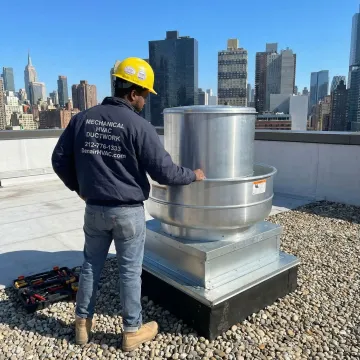 HVAC technician inspecting a roof exhaust fan on a building in Long Island City