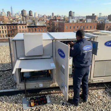 Certified technician repairing a Carrier HVAC unit on a Brooklyn rooftop