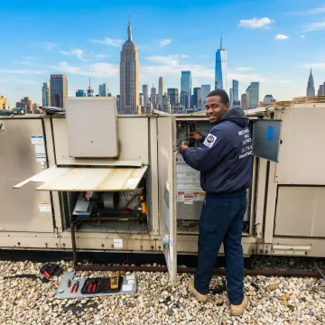 HVAC technician performing maintenance on a rooftop unit in Queens, NY