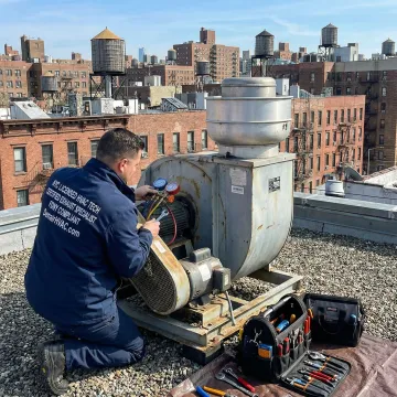 HVAC technician repairing a roof exhaust fan on a Queens, NY building rooftop