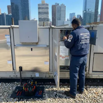 Commercial HVAC technician performing scheduled maintenance on rooftop unit in Queens, NY