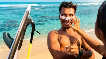 Surfer applying reef-safe mineral sunscreen before entering ocean water