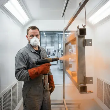 Industrial powder coating technician applying thermoset finish to a metal fabricated part