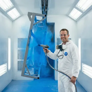 Technician applying powder coating to a metal fabricated part in an industrial facility