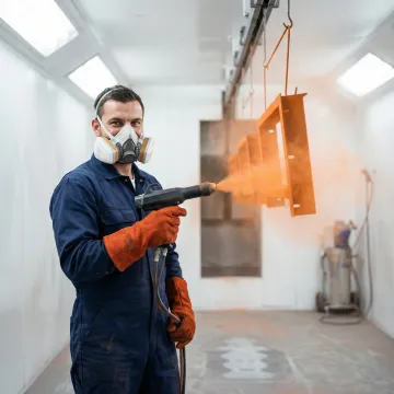Technician applying powder coating to a custom metal part in an industrial facility