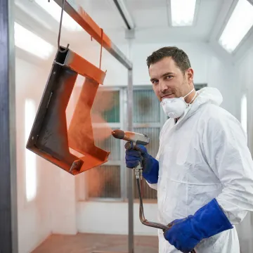Technician applying powder coating finish to a metal fabricated assembly in an industrial shop
