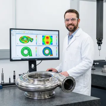 Engineer reviewing CMM coordinate measurement data on a computer screen next to a machined aerospace component