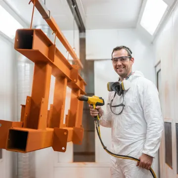 Industrial powder coating technician applying thermoset powder finish to a fabricated metal assembly