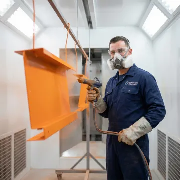 Technician applying powder coating to a metal fabricated assembly in an industrial paint shop