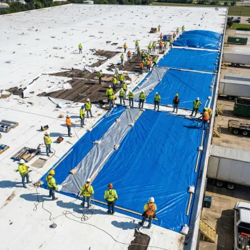 Emergency commercial roof repair crew securing damaged roof during storm conditions