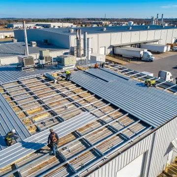 Roofing crew installing metal retrofit panels on a commercial roof