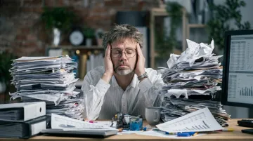 Tired executive showing decision fatigue at desk with multiple documents and screens