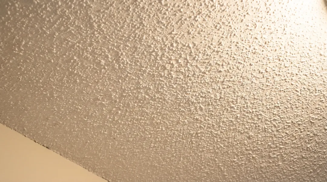 Close-up photograph of a white textured popcorn ceiling in an older home