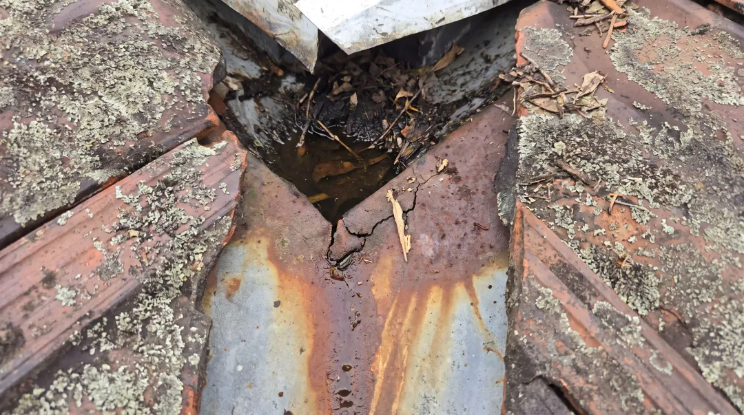 Cracked rusted valley flashing with debris causing roof leak