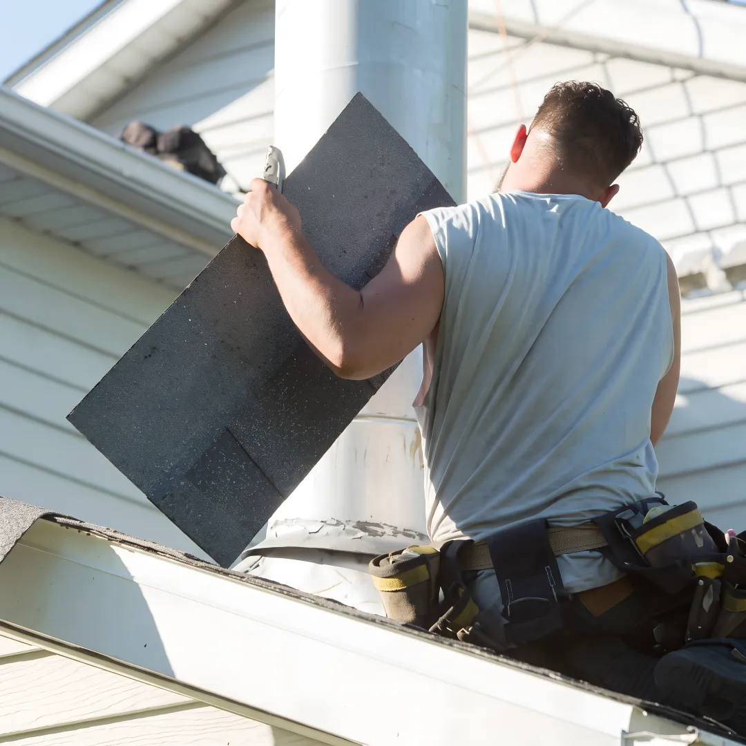 Roofing technician repairing shingles near a roof vent