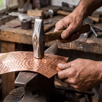 Artisan hammering a textured copper sheet