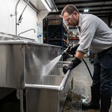 A worker cleaning equipment in a heavy-duty sink at a food processing plant.