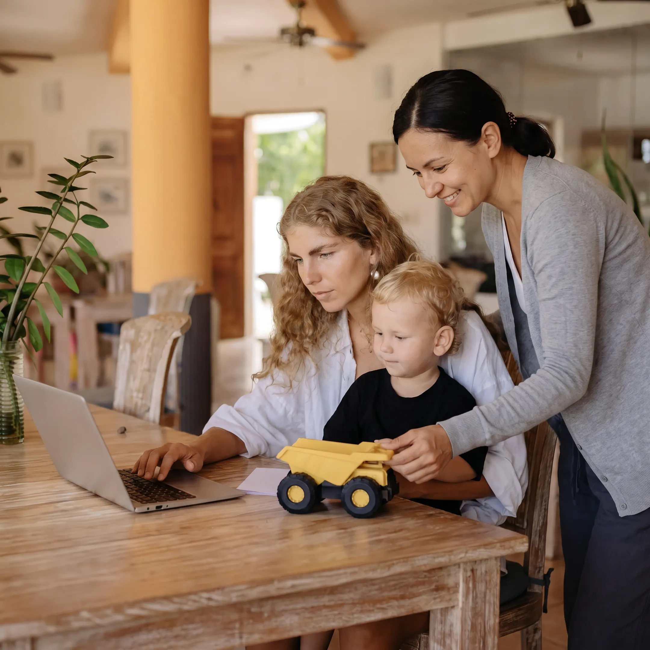 Working mother collaborating on laptop while child plays safely nearby