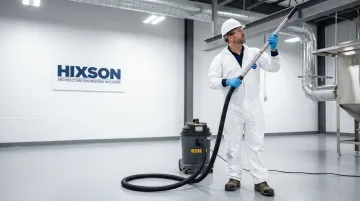 Industrial worker using Class II vacuum system to clean combustible dust from facility floor and beams