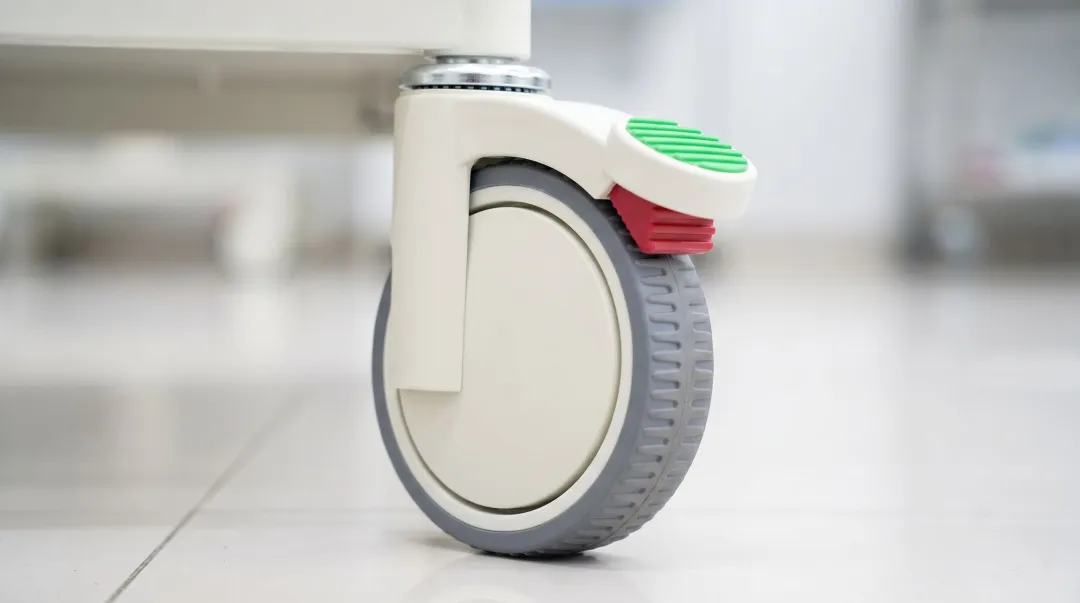 Hospital equipment caster with visible wear debris buildup and brake mechanism detail