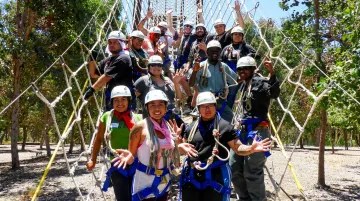 Corporate team completing outdoor adventure course aerial obstacles together