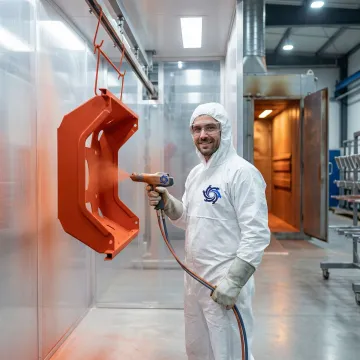 Industrial powder coating technician applying uniform finish to metal fabricated components in a manufacturing facility