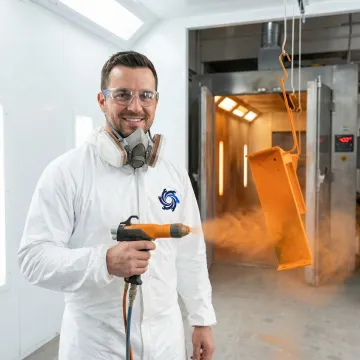 Industrial powder coating technician applying uniform finish to metal components in a professional facility