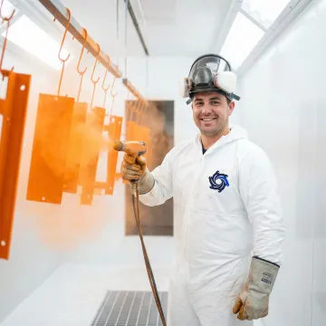 Technician applying powder coating to a metal component in an industrial facility