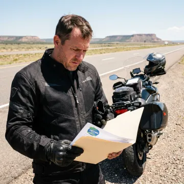 Motorcyclist reviewing insurance documents beside a bike