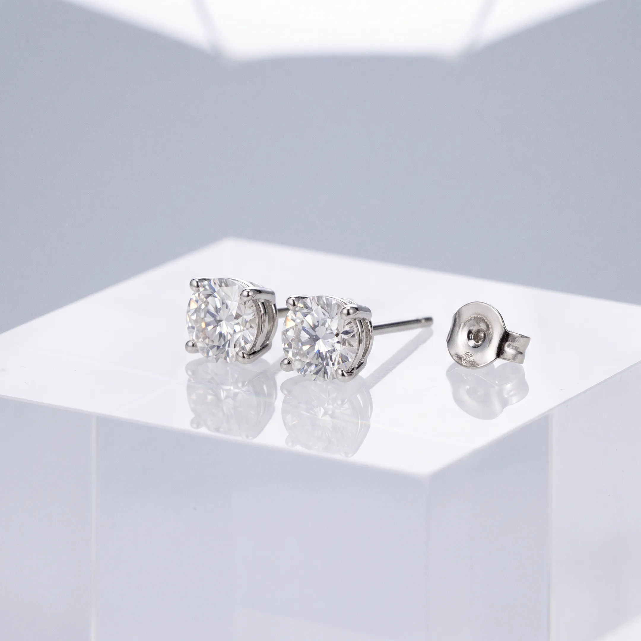 Studio jewelry photograph of diamond earrings displayed on clean acrylic background.