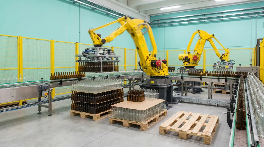Industrial robotic palletizing cell with multiple articulated robots handling glass bottles