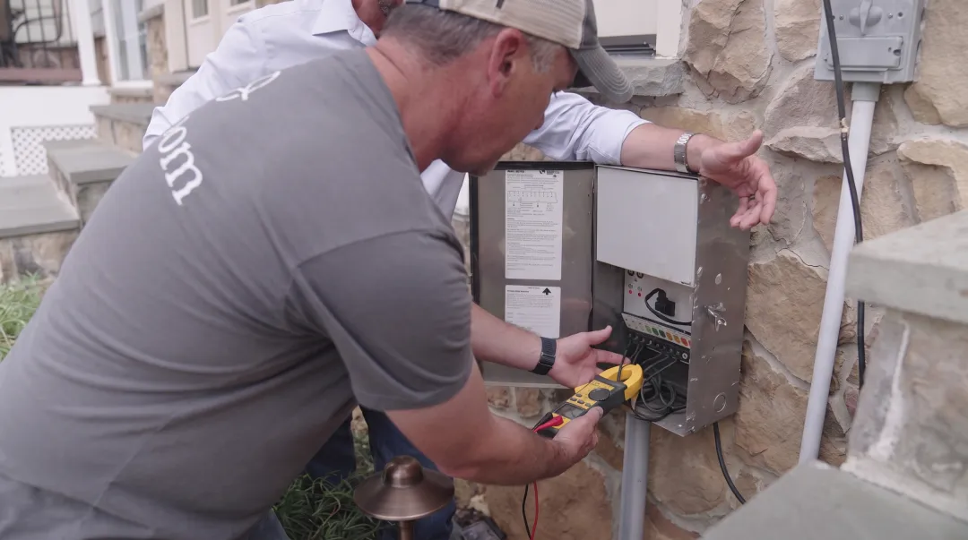 Professional landscape lighting technician inspecting outdoor fixture connections and transformer system