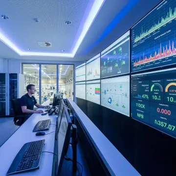 Engineer monitoring real-time manufacturing data on screens showing networked equipment status