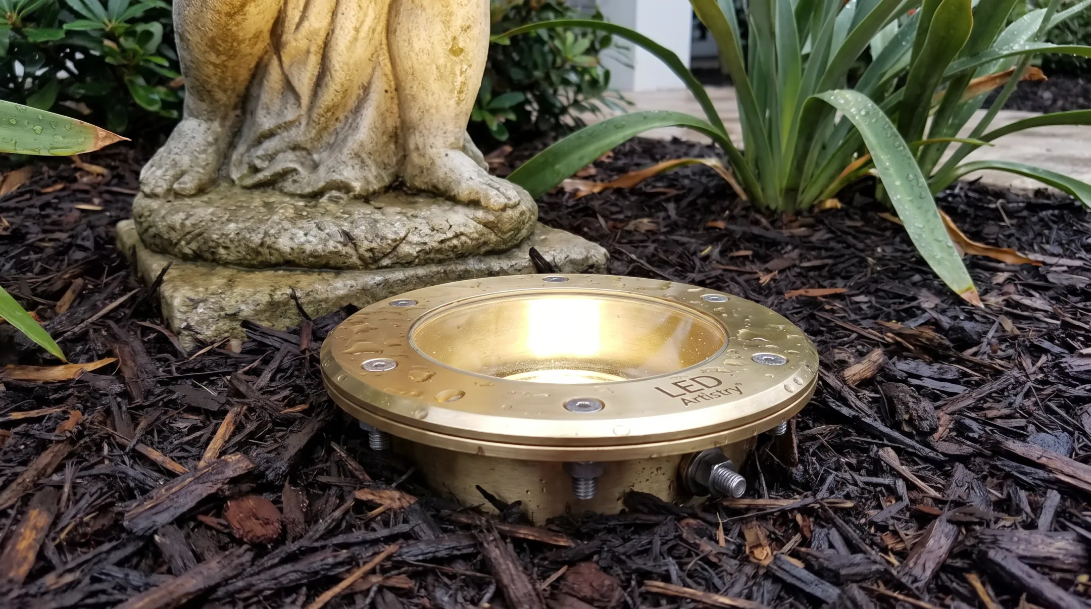 Brass ground-recessed fixture illuminating garden statue in Florida landscape
