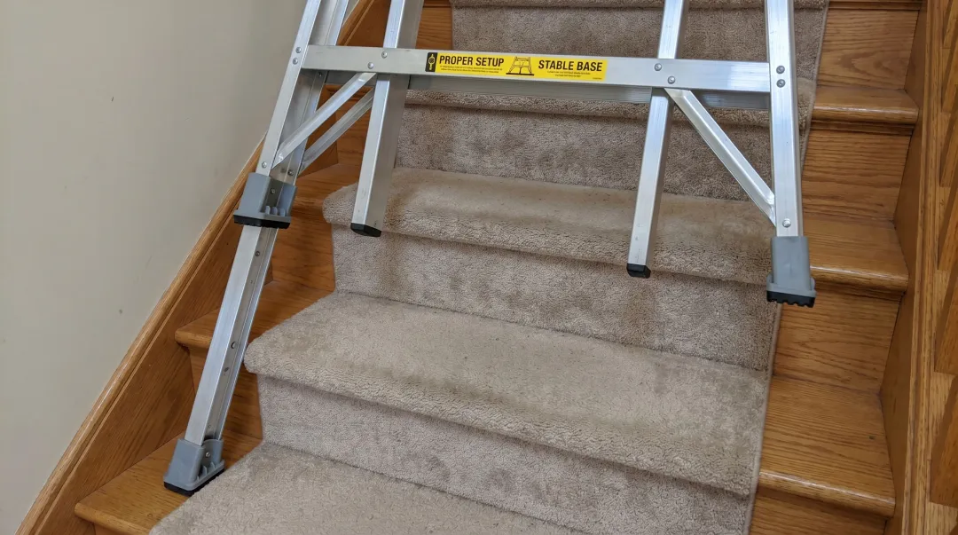 Ladder leveling device properly positioned on carpeted staircase treads