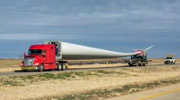 Specialized extendable blade trailer with articulating rear dolly transporting wind turbine blade on highway