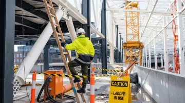 Worker on ladder near electrical hazard with safety barricade at worksite
