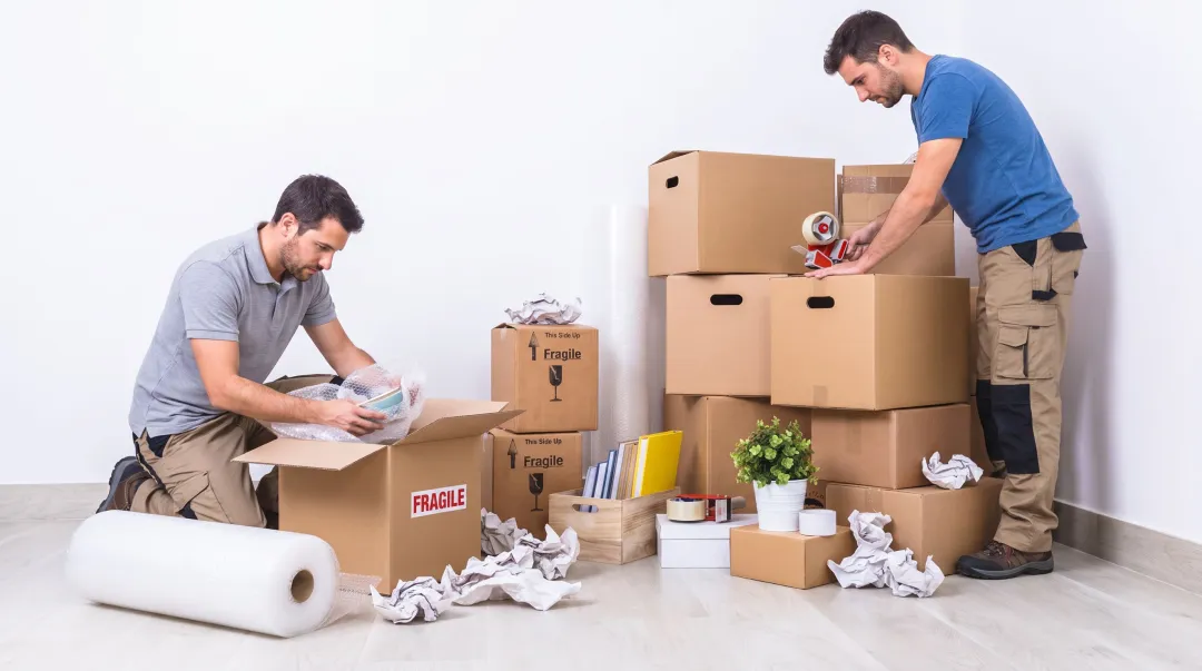 Professional movers carefully packing and wrapping household items with protective materials in boxes