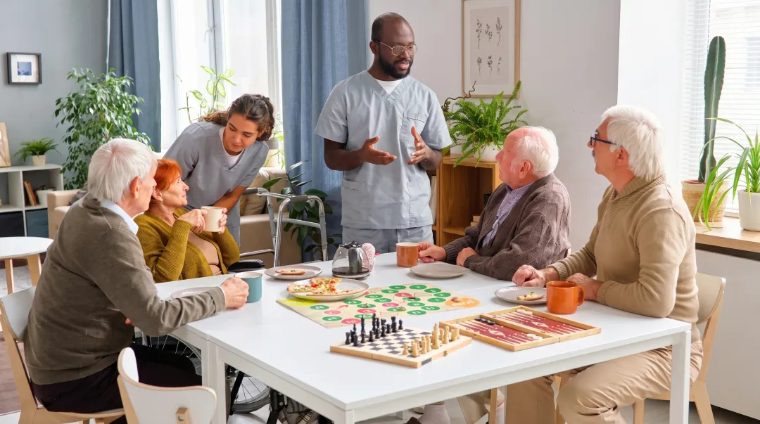 Senior living community common area with residents engaged in social activities and staff interaction