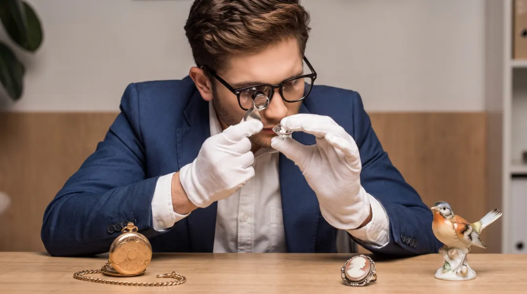 Professional appraiser examining antique jewelry and collectibles with magnifying loupe