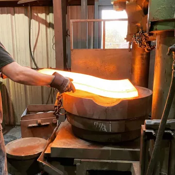 Hot drape forming process shaping a heated metal plate over a die in an industrial forge facility