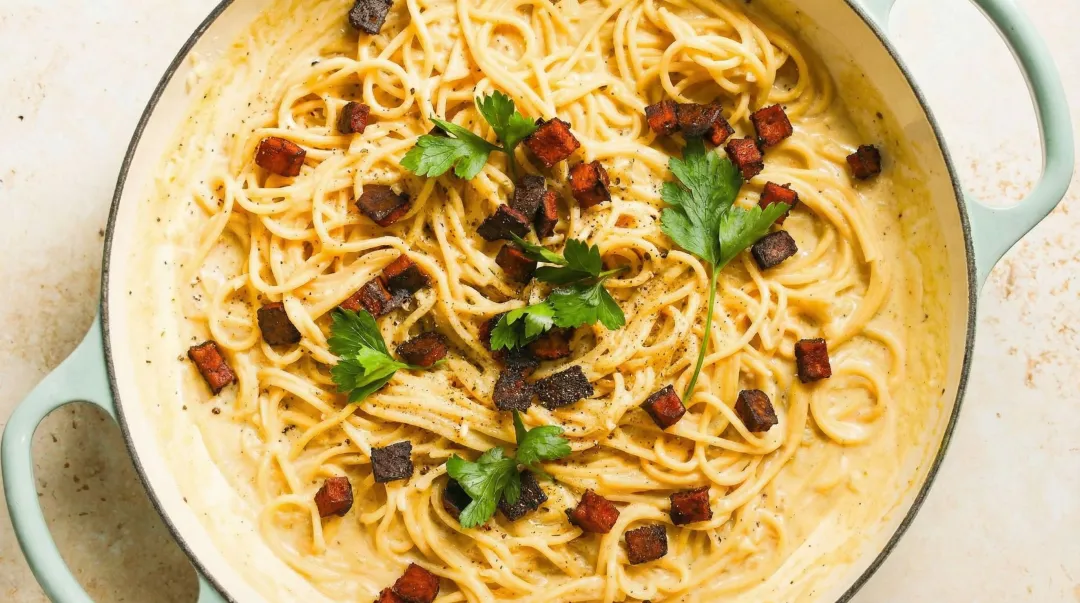 Creamy vegan pasta carbonara in skillet with smoky tofu and parsley garnish