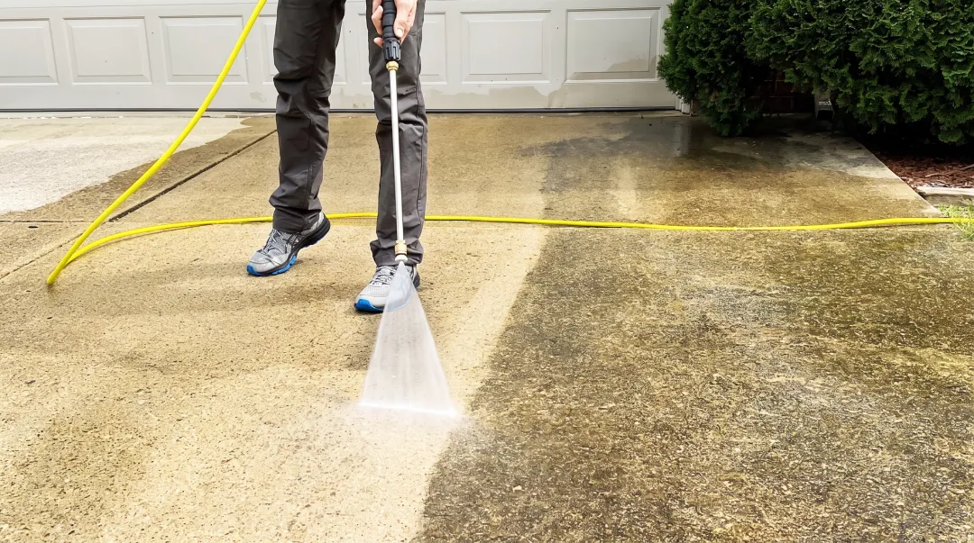 Professional pressure washing concrete driveway removing embedded dirt and tire marks