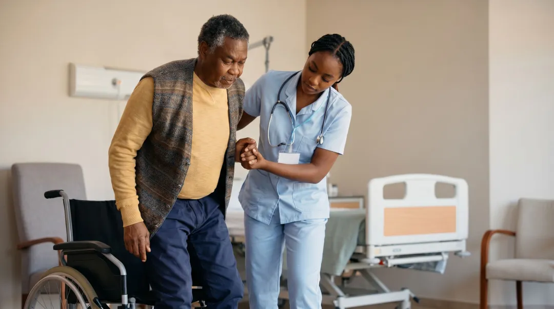 Nursing home worker assisting elderly resident in long-term care facility hallway