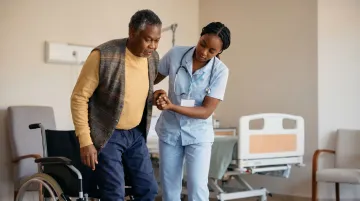 Nursing home worker assisting elderly resident in long-term care facility hallway