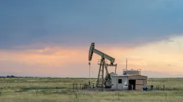 Oil pumpjack and drilling rig operating in Colorado plains landscape